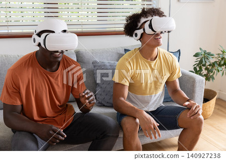 Diverse male friends sitting on sofa in living room wearing vr headsets exploring vr world Diverse male friends sitting on sofa in living room wearing vr headsets exploring vr world 140927238