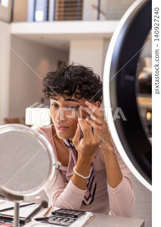 Man applying eyeliner while using mirror under ring light with palettes in living area Man applying eyeliner while using mirror under ring light with palettes in living area 140927240