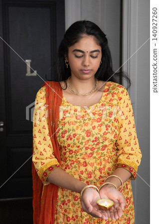 Indian woman wearing gold jewelry standing by door l in hallway holding clay oil lamp Indian woman wearing gold jewelry standing by door l in hallway holding clay oil lamp 140927260