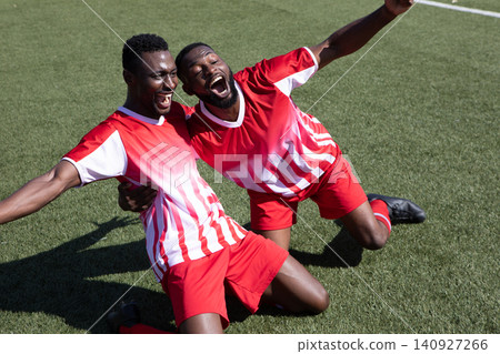 African American male teammates shouting while kneeling on turf wearing striped jerseys and cleats African American male teammates shouting while kneeling on turf wearing striped jerseys and cleats 140927266