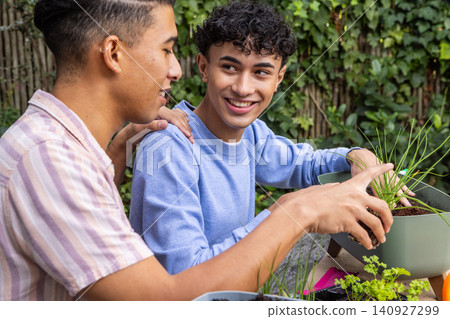 Male friends filling planter with soil, placing herb seedlings on backyard garden table Male friends filling planter with soil, placing herb seedlings on backyard garden table 140927299