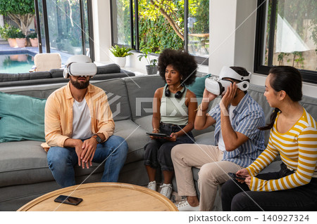 Diverse friends sitting on sofa in living room using vr headsets and holding tablet smartphone 140927324