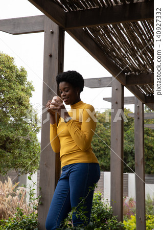 African american woman standing under pergola in garden with ceramic mug with wristwatch visible African american woman standing under pergola in garden with ceramic mug with wristwatch visible 140927332