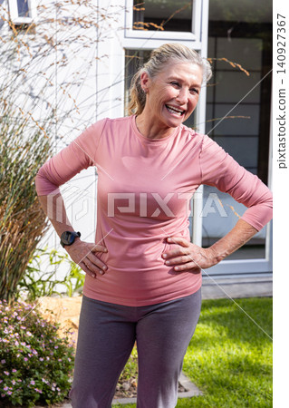 Senior woman standing with hands on hips in backyard garden wearing athletic outfit Senior woman standing with hands on hips in backyard garden wearing athletic outfit 140927367