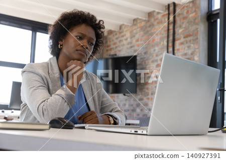 Mid adult african american woman sitting at desk in office using laptop with mouse, notebook Mid adult african american woman sitting at desk in office using laptop with mouse, notebook 140927391