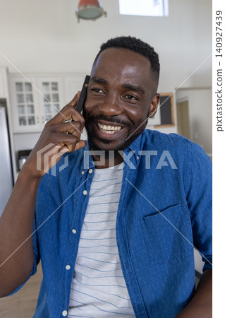 African american man talking on smartphone while leaning in bright kitchen African american man talking on smartphone while leaning in bright kitchen 140927439