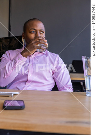 African american man sipping from tumbler at office desk with laptop, copy space African american man sipping from tumbler at office desk with laptop, copy space 140927448