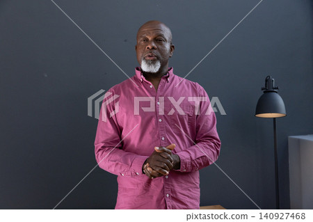 Senior african american man addressing audience in studio near gray wall with lamp and table Senior african american man addressing audience in studio near gray wall with lamp and table 140927468