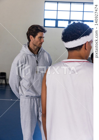 Male coach and african american player practicing on gym court with whistle, bench, copy space Male coach and african american player practicing on gym court with whistle, bench, copy space 140927474