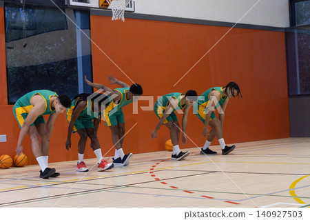 Diverse male basketball teammates reaching toward floor on court with basketballs and hoop Diverse male basketball teammates reaching toward floor on court with basketballs and hoop 140927503