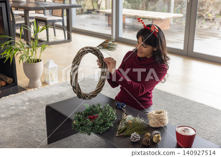Woman wearing sweater sitting on home floor assembling wreath with vine base, twine, copy space Woman wearing sweater sitting on home floor assembling wreath with vine base, twine, copy space 140927514
