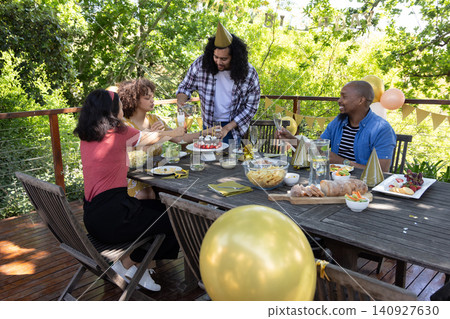 Diverse friends gathering around table on deck, toasting wine glasses, strawberry cake Diverse friends gathering around table on deck, toasting wine glasses, strawberry cake 140927630