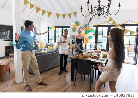 Diverse friends gathering around dining table laughing and pointing at cake in living room Diverse friends gathering around dining table laughing and pointing at cake in living room 140927638
