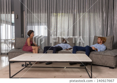 Diverse friends relaxing on gray sectional sofa in living room with wood coffee table Diverse friends relaxing on gray sectional sofa in living room with wood coffee table 140927667