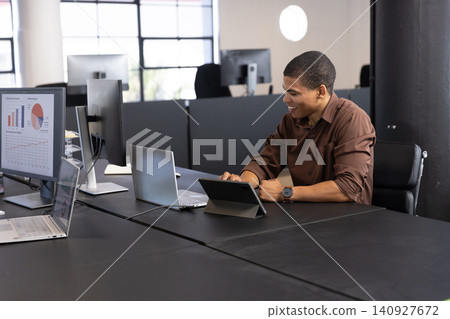African american man typing on tablet as monitor displaying charts at office, copy space African american man typing on tablet as monitor displaying charts at office, copy space 140927672