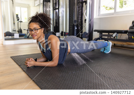 African American woman holding forearm plank on textured mat in home gym with weight machines African American woman holding forearm plank on textured mat in home gym with weight machines 140927712