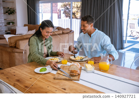 Diverse couple eating breakfast at home dining table with scrambled eggs, orange juice Diverse couple eating breakfast at home dining table with scrambled eggs, orange juice 140927721