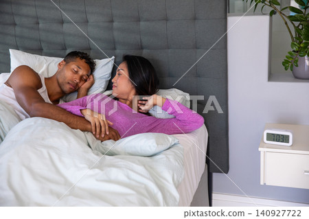 African american man lying shirtless and asian woman in pink top under white comforter on bed African american man lying shirtless and asian woman in pink top under white comforter on bed 140927722