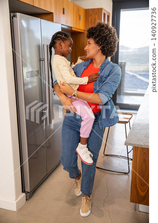 African american mother with daughter holding hands in kitchen by kitchen island with window view 140927736