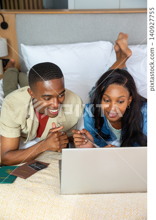 African American couple lying on bed in bedroom planning trip using laptop, passports and stylus African American couple lying on bed in bedroom planning trip using laptop, passports and stylus 140927755