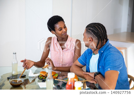 African American couple sitting at glass dining table in kitchen preparing burgers with smartphone African American couple sitting at glass dining table in kitchen preparing burgers with smartphone 140927756