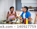 African American and Hispanic couple eating burgers at kitchen table with salad, condiment bottles 140927759