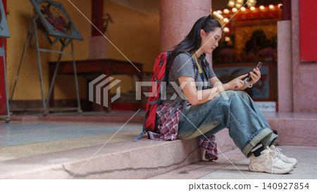 Asian woman tourist sitting on temple steps and using smartphone for navigation Asian woman tourist sitting on temple steps and using smartphone for navigation 140927854