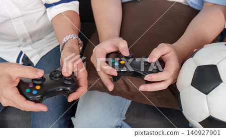 Cropped hands of family members playing soccer video game with controllers at home 140927901