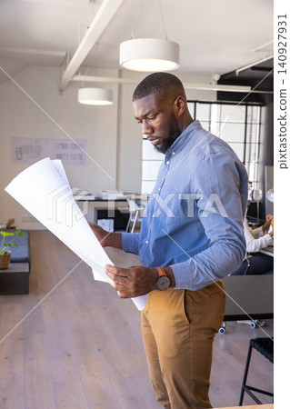 African american man standing, examining blueprints at office desk in workspace, copy space African american man standing, examining blueprints at office desk in workspace, copy space 140927931