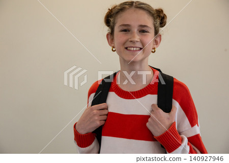 Female child student smiling and holding black backpack straps against wall, copy space Female child student smiling and holding black backpack straps against wall, copy space 140927946