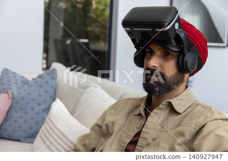 Indian man wearing vr headset sitting in living room by sliding glass door, copy space Indian man wearing vr headset sitting in living room by sliding glass door, copy space 140927947