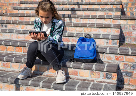 Girl student sitting on outdoor brick steps using touchscreen device with backpack, copy space Girl student sitting on outdoor brick steps using touchscreen device with backpack, copy space 140927949
