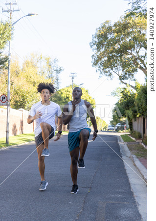 Diverse male friends running high-knee drills wearing fitness watches on street Diverse male friends running high-knee drills wearing fitness watches on street 140927974