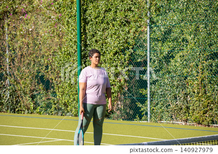 African american woman standing on court and holding racket in lavender shirt leggings with net 140927979