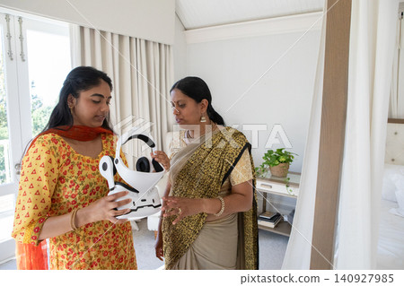 Indian mother and daughter in traditional dress while examining virtual reality headset in room Indian mother and daughter in traditional dress while examining virtual reality headset in room 140927985