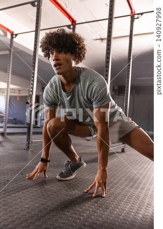 African American man in sportswear doing lunge stretch in gym on rubber flooring near squat racks African American man in sportswear doing lunge stretch in gym on rubber flooring near squat racks 140927998