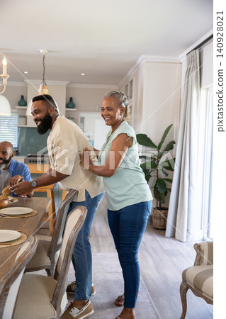 African American family preparing meal in modern kitchen at wooden dining table with covered dish 140928021