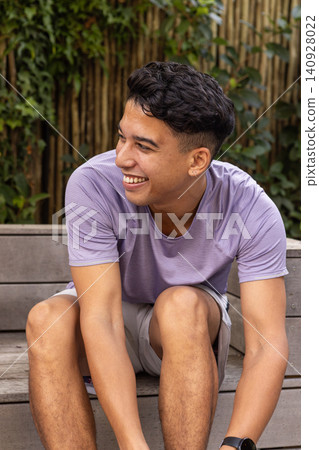 Man wearing sportswear sitting on wooden bench in garden leaning smiling with smartwatch Man wearing sportswear sitting on wooden bench in garden leaning smiling with smartwatch 140928022