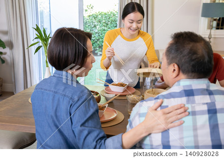 Diverse family serving noodles from bamboo steamer around, dining table in home dining room 140928028