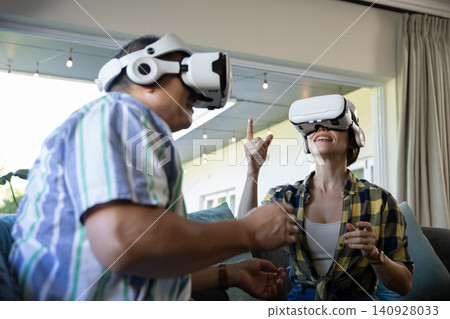 Senior couple experiencing virtual reality on two-seater sofa in living room with vr headsets Senior couple experiencing virtual reality on two-seater sofa in living room with vr headsets 140928033