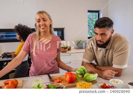 Diverse friends slicing bell peppers on cutting board in home kitchen Diverse friends slicing bell peppers on cutting board in home kitchen 140928040