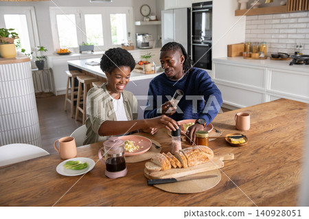 African american couple seasoning scrambled eggs with pepper and salt grinders at table in kitchen 140928051