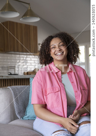 African American woman smiling and sitting on sofa in open-plan kitchen with cabinets brass lights African American woman smiling and sitting on sofa in open-plan kitchen with cabinets brass lights 140928055