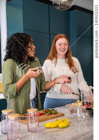 Diverse female friends chopping fruit on marble kitchen island with blender pitcher Diverse female friends chopping fruit on marble kitchen island with blender pitcher 140928101