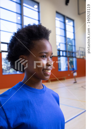African american teenage girl smiling, looking right in gym by basketball court lines African american teenage girl smiling, looking right in gym by basketball court lines 140928119