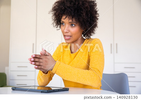 African american woman in yellow top at home office against cabinets with tablet 140928130