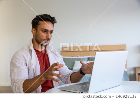 Man gesturing in meeting at bedroom table with laptop beside bed frame Man gesturing in meeting at bedroom table with laptop beside bed frame 140928132