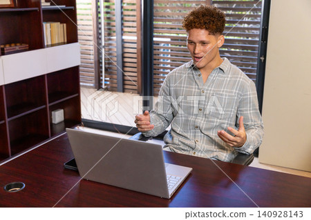 White male sitting at home office desk gesturing during online call with laptop White male sitting at home office desk gesturing during online call with laptop 140928143