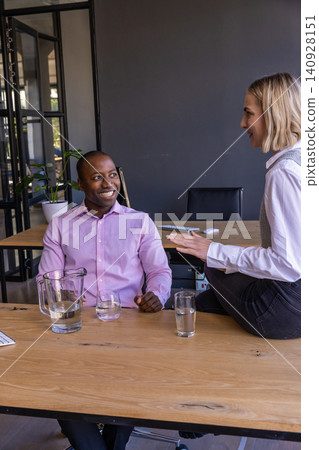 Diverse coworkers in office attire discussing plan in meeting room with table, water pitcher Diverse coworkers in office attire discussing plan in meeting room with table, water pitcher 140928151