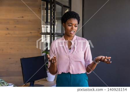 African american woman gesturing and speaking at office desk, laptop and plant 140928154